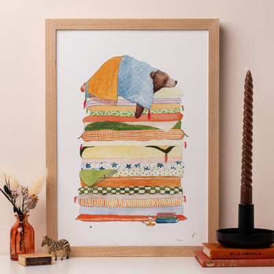 A framed print of a drawing of a bear sleeping of a pile of mattresses