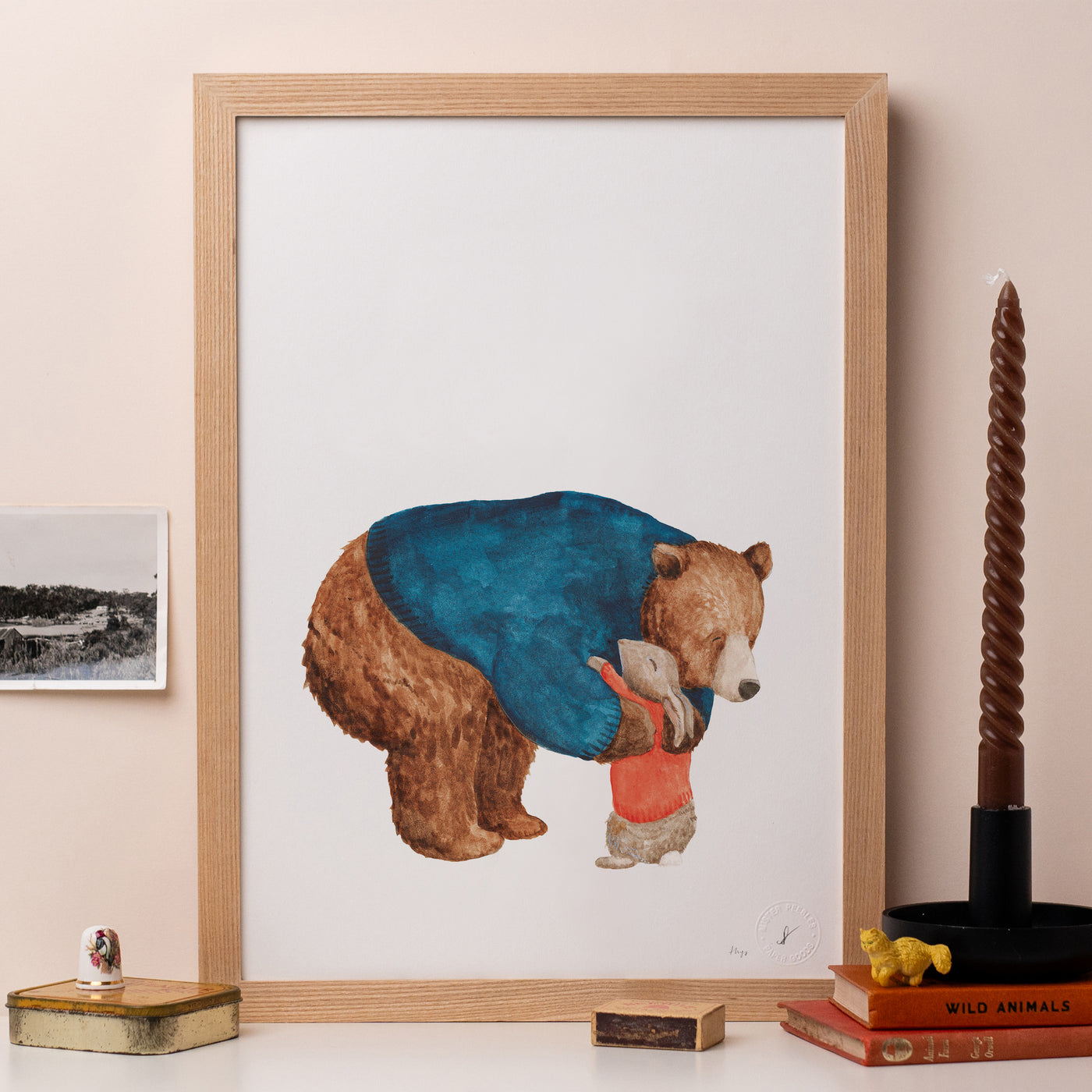 A framed print of a drawing of a brown bear hugging a rabbit.