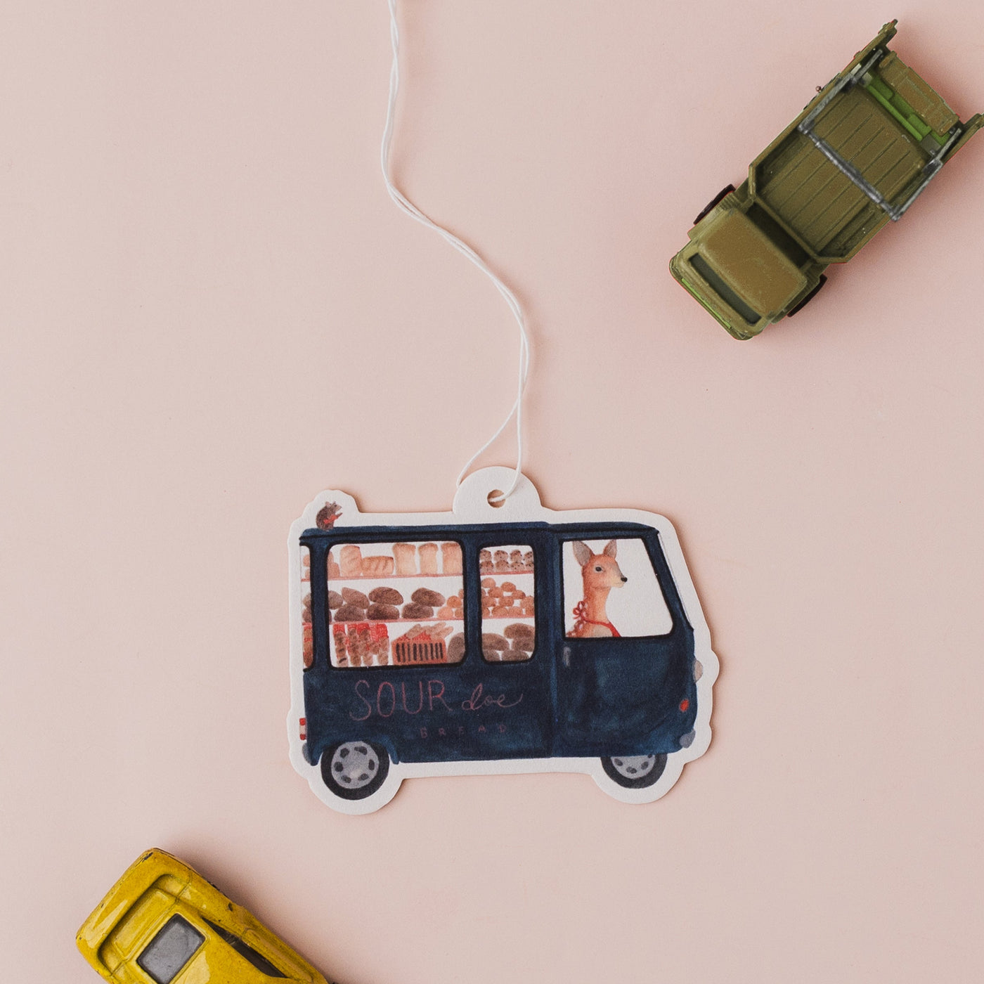 Decorative car-shaped air freshener with a string on a pink background
