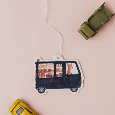 Decorative car-shaped air freshener with a string on a pink background