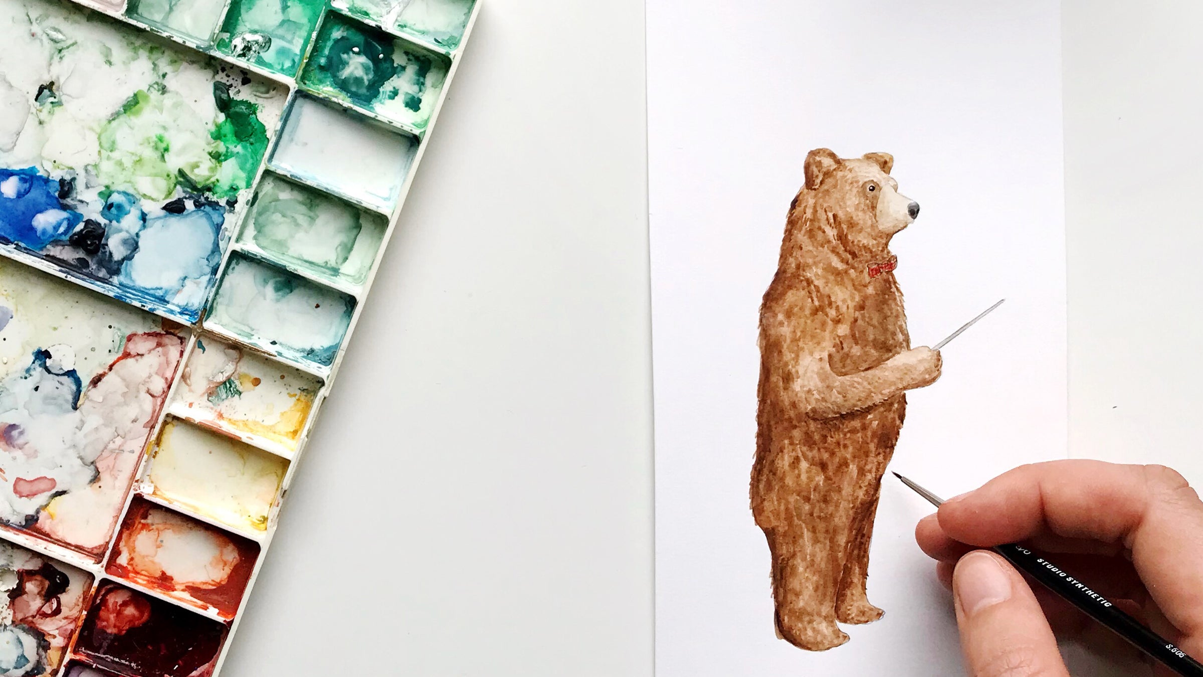 A hand painting a bear illustration with a watercolour paint palette