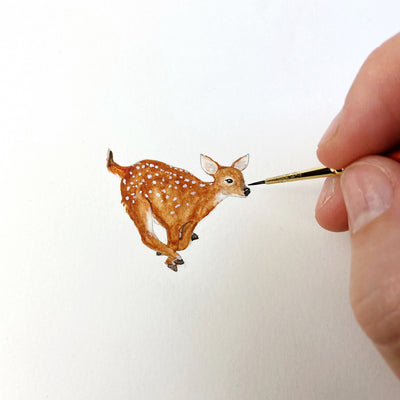 A hand painting a small drawing of a baby deer