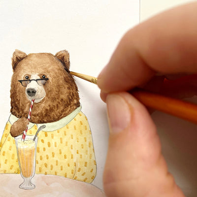 A hand painting a watercolour illustration of a bear